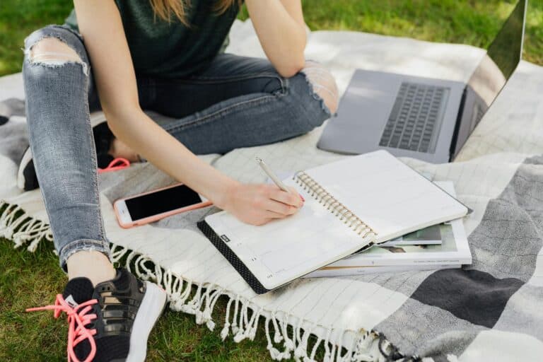 A person sitting on a blanket writing in a notebook.